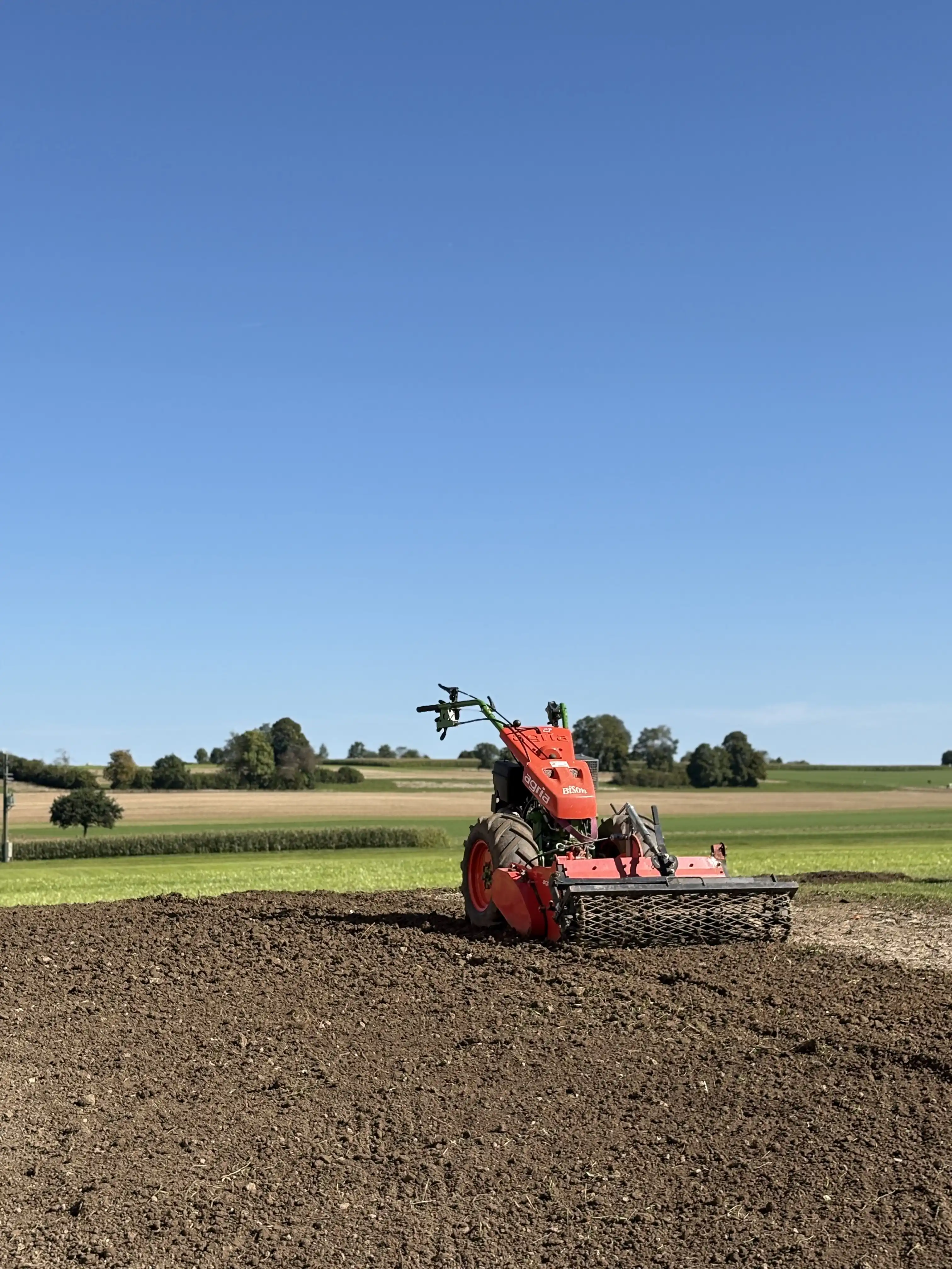 Motoculteur avec herse rotative sur une grande surface de terre préparée, campagne et ciel bleu