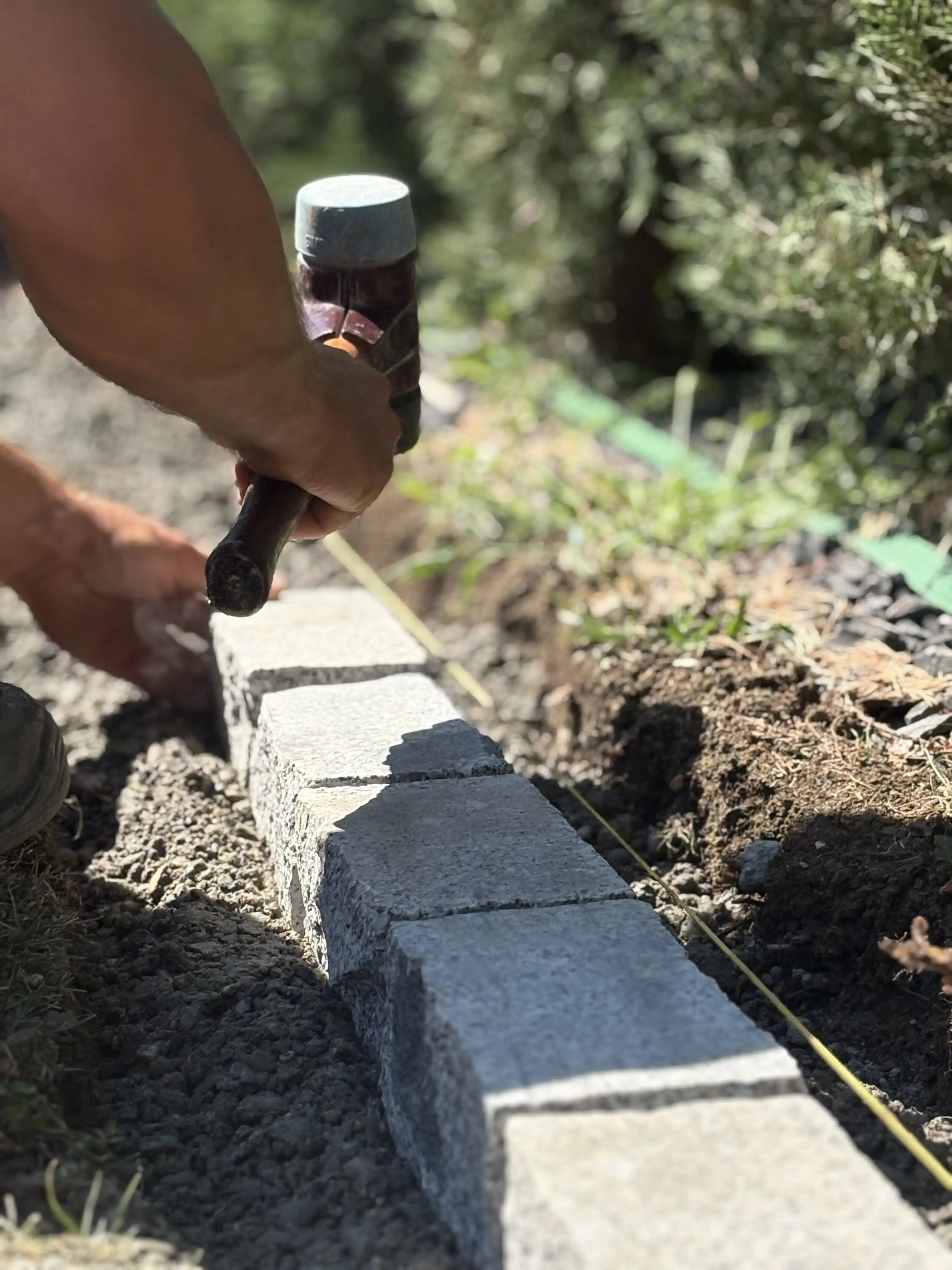 Pose d'une bordure : un pavé calé au maillet le long d'un cordeau tendu